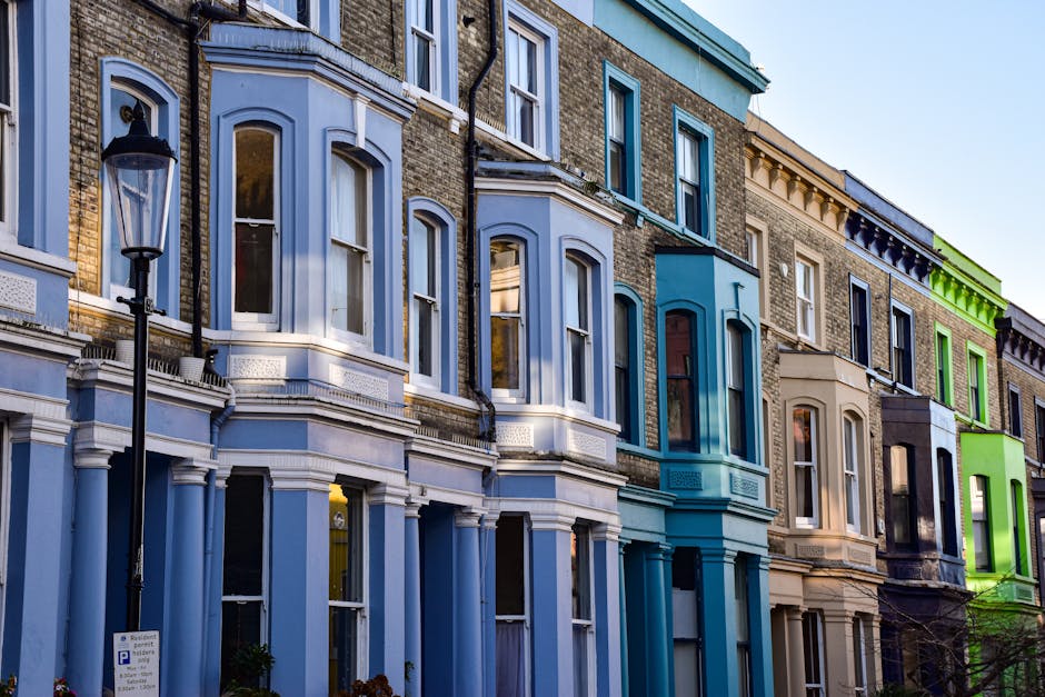 A row of Victorian terraced houses featuring distinctive bay windows with white trim and decorative mouldings. The façades are painted in various pastel shades, including turquoise, white, light blue