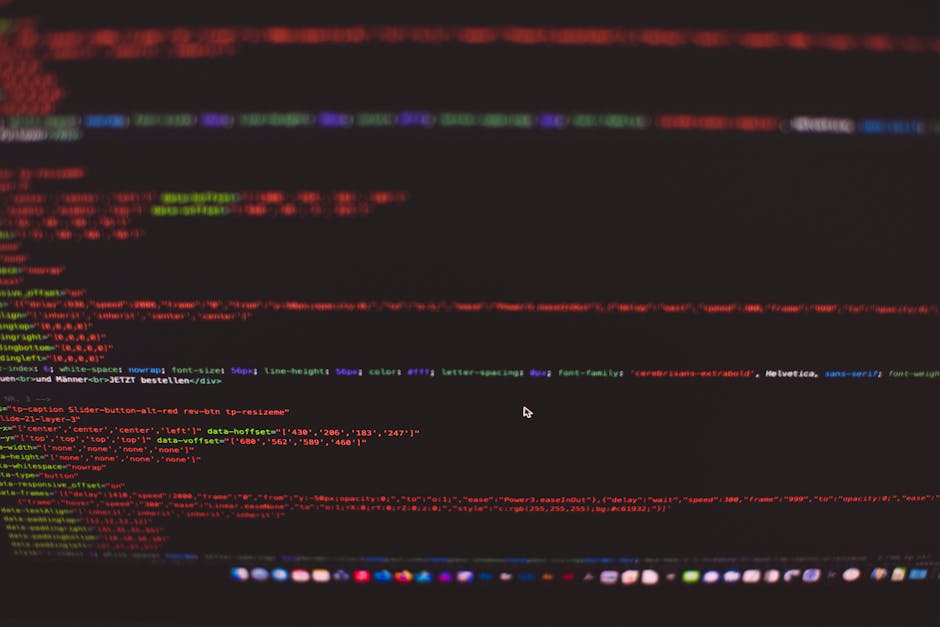 A computer screen displaying lines of colorful programming code, including syntax with functions, variables, and comments, on a dark background. The monitor is positioned at an angle, revealing a slig
